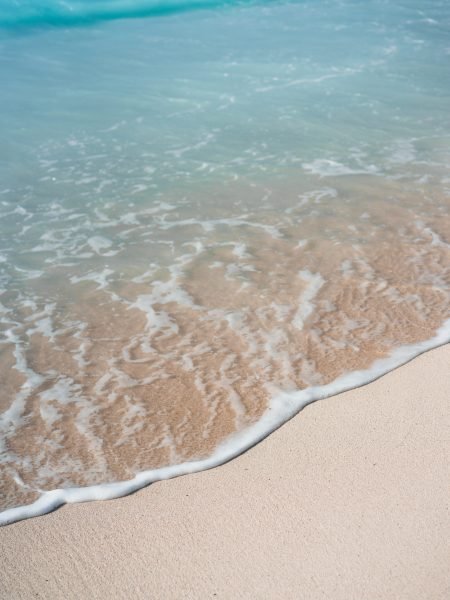 Blue transparent ocean wave rolling to sandy beach with azure water. White wave foam in front.