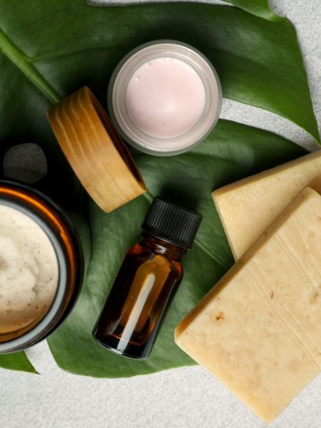 Different body care products and monstera leaf on light grey table, top view